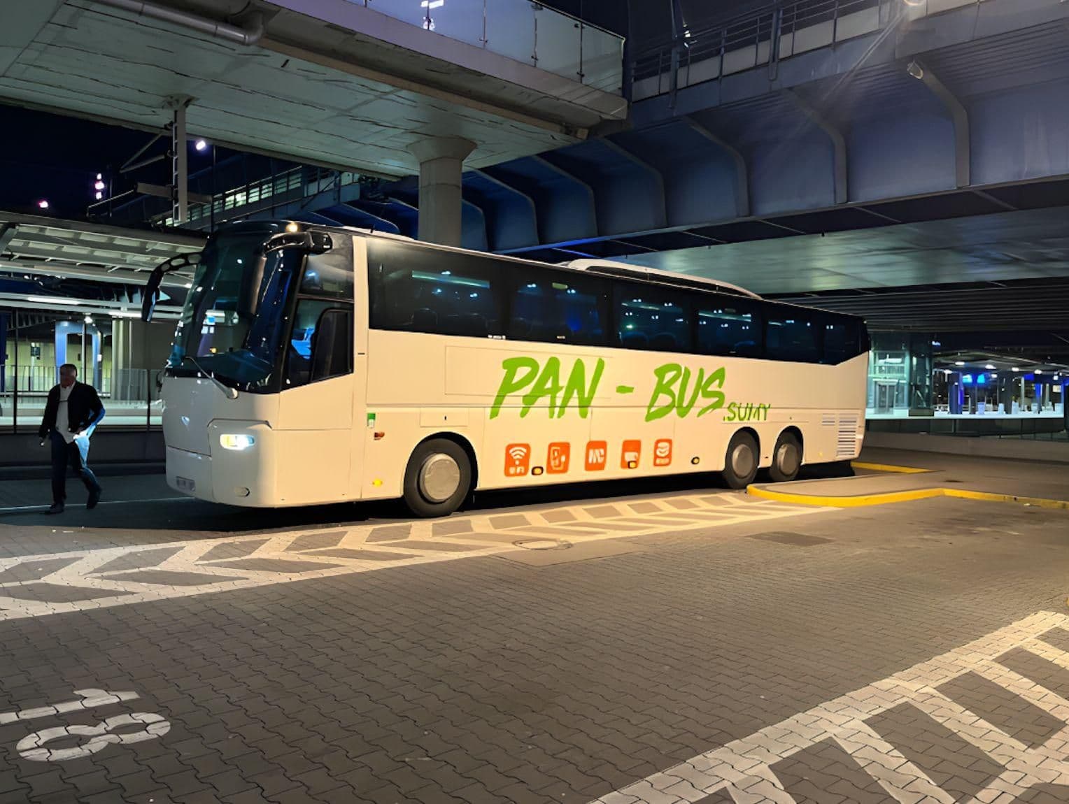 Автобус перевізника PAN-BUS на автовокзалі в нічний час, сучасний білий туристичний автобус з логотипом компанії, підготовлений до міжнародного рейсу.
