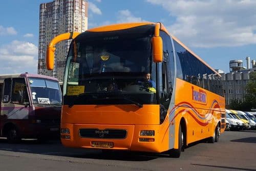 Помаранчевий VIP-лайнер TransTempo MAN Lion’s Star (R03) класу Euro-3, припаркований у місті біля висотного житлового будинку автовокзалу — зручне бронювання квитків на atatickets.com.