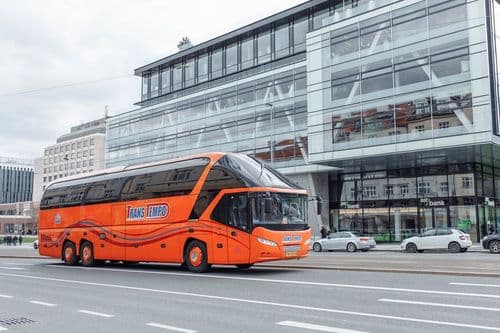 VIP-автобус Neoplan Starliner L перевізника TransTempo біля сучасного готельного комплексу — бронювання квитків на міжнародні рейси на atatickets.com.