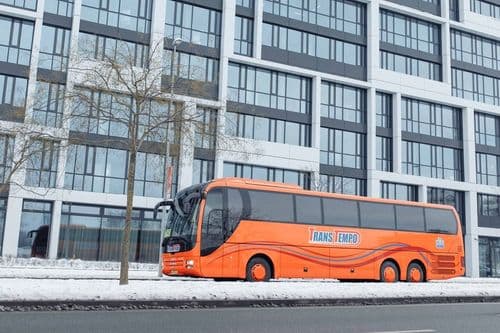 Помаранчевий автобус MAN Lion’s Coach перевізника ТрансТемпо на засніженій вулиці біля білого офісу на atatickets.com.