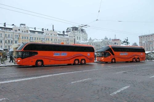 Два помаранчеві лайнери TransTempo на засніженій площі в центрі міста — зручний розклад та квитки на міжнародні рейси через сервіс atatickets.com.