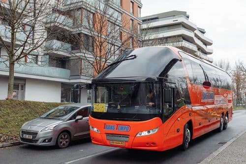 Сучасний автобус TransTempo моделі Neoplan Starliner C на фоні міської забудови — зручне бронювання квитків на міжнародні рейси через atatickets.com.