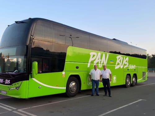 Зелений туристичний автобус перевізника PAN-BUS на парковці, сучасний міжміський автобус із фірмовим брендуванням та екіпажем поруч, що виконує міжнародні пасажирські рейси.